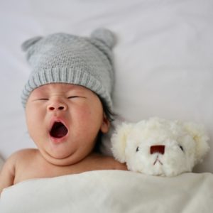 tiny baby yawning in bed with white teddy and yawning