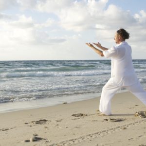 man in tai qi whites practicing qi gong by the sea