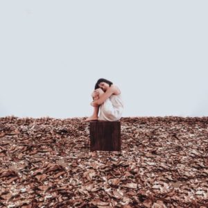 solitary girl sitting on block of wood on wasteland